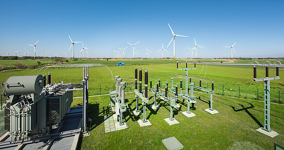 Substation in a green field with wind turbines in the background