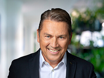 Man with short brown hair, dark jacket, and white shirt