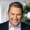 Mann mit kurzen dunklen Haaren, blauen Augen, schwarzem Jackett und weißem Hemd