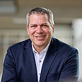 Man with short gray hair, brown eyes, dark blue jacket, and white shirt