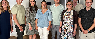 Gruppenfoto mit acht Personen - vier Frauen und vier Männern. Alle lächeln freundlich in die Kamera.