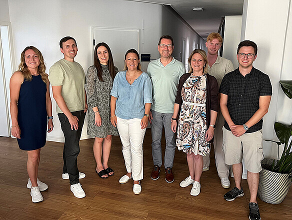 Group photo with eight people—four women and four men. Everyone is smiling warmly at the camera.
