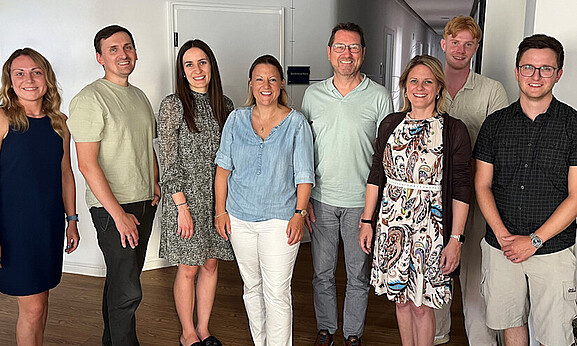 Gruppenfoto mit acht Personen - vier Frauen und vier Männern. Alle lächeln freundlich in die Kamera.