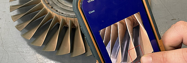 Eine Person erfasst per Smartphone einen Befund an einer Turbinenschaufel. 
