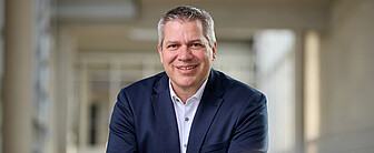 Mann mit kurzen grauen Haaren, braunen Augen, dunkelbauen Jackett und weißem Hemd