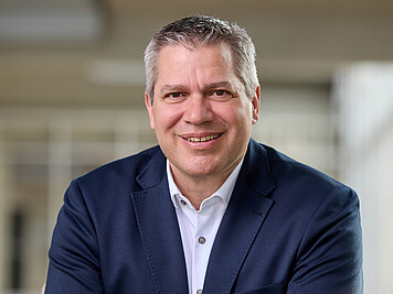 Man with short gray hair, brown eyes, dark blue jacket, and white shirt