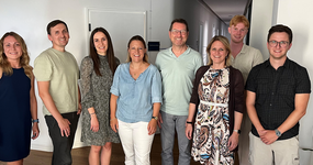 Gruppenfoto mit acht Personen - vier Frauen und vier Männern. Alle lächeln freundlich in die Kamera.