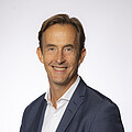 Man in a blue jacket and white shirt with short blond hair